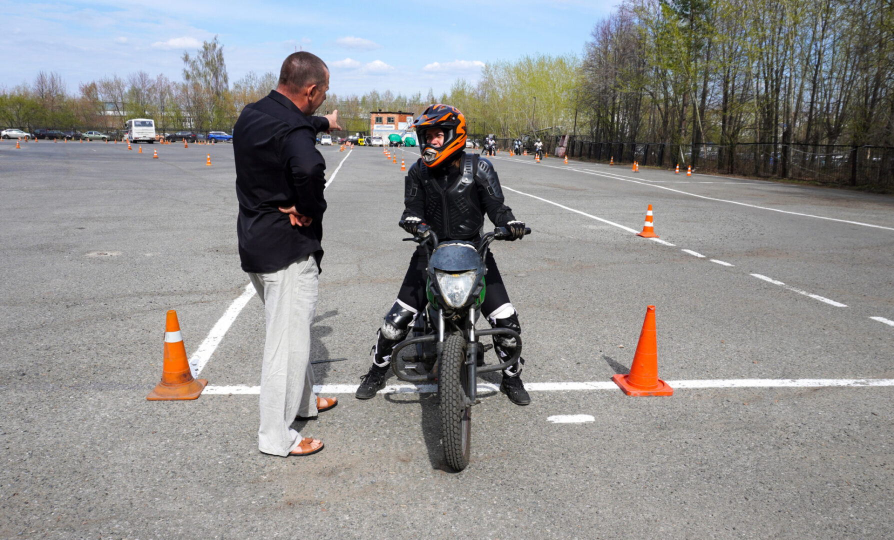 A young woman is learning to ride a motorbike in a motorcycle school. She is taught by a teacher.
